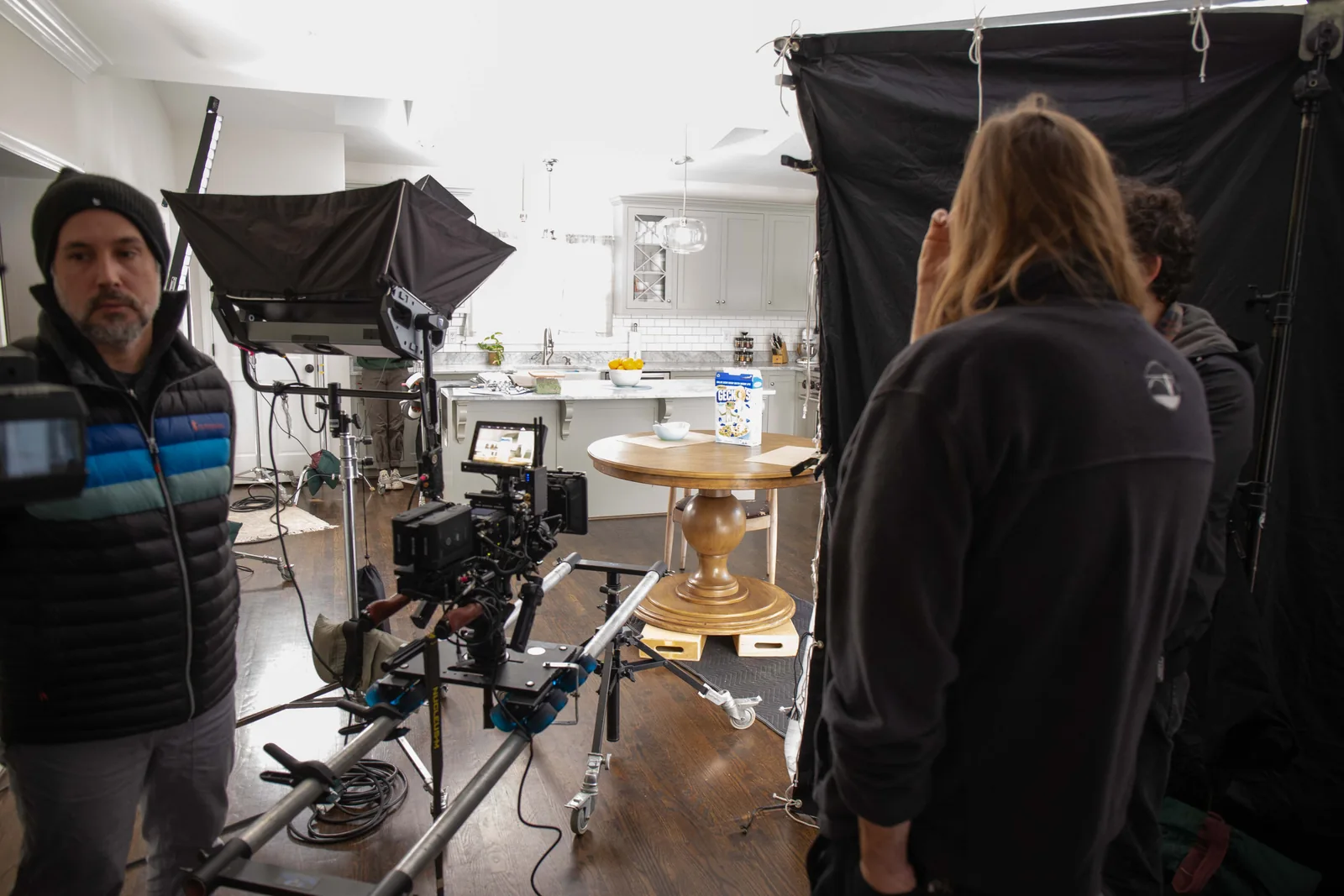 Camera rig and crew in the kitchen set, with the breakfast table and lighting equipment visible.