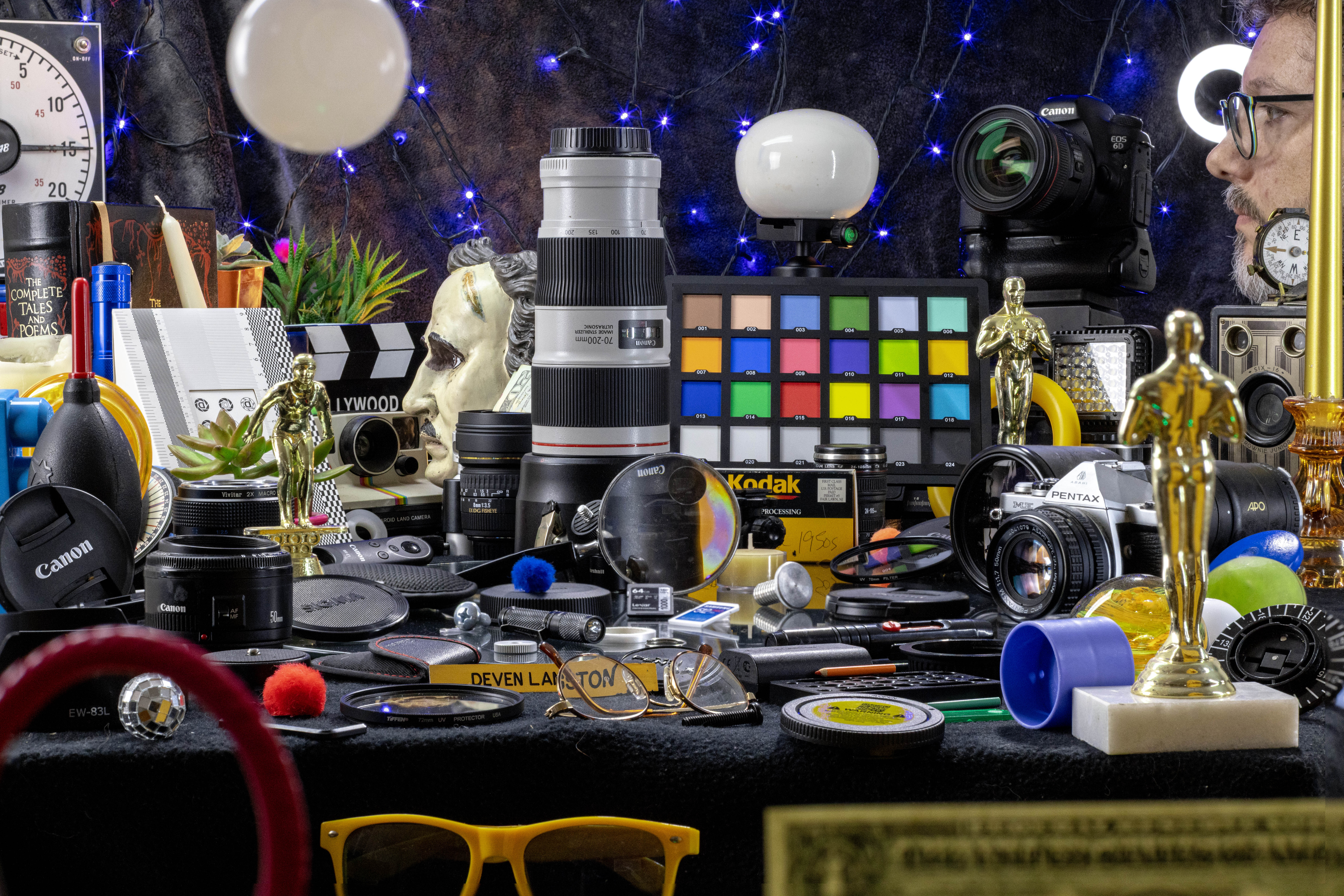 Deven in profile beside a colorful arrangement of cameras and creative objects
